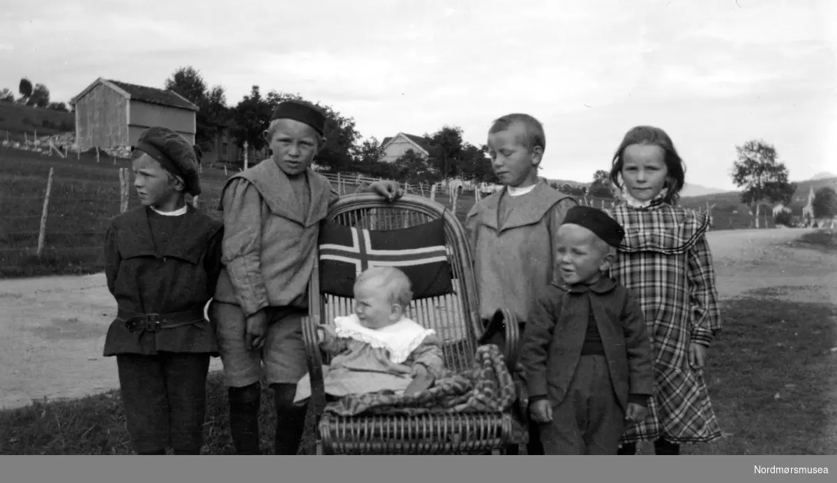 Gruppe på seks barn, hvorav den minste sitter i en flaggprydet barnevogn. Barna
 er de 6 første barna til Margrethe Sverdrup og Georg Sverdrup., Litt usikkert hvem er hvem, men piken helt til høyre er Hildur, minstebarnet i stolen er Kaare , og foran Hildur står Olaf. De andre er Georg, Henrik, og Helge. Bildet er tatt i Eidsvågen, Nesset kommune.Møre og Romsdal fylke. Datering er ukjent, men trolig omkring 1900 til 1910.
Fra Nordmøre museums fotosamlinger.
