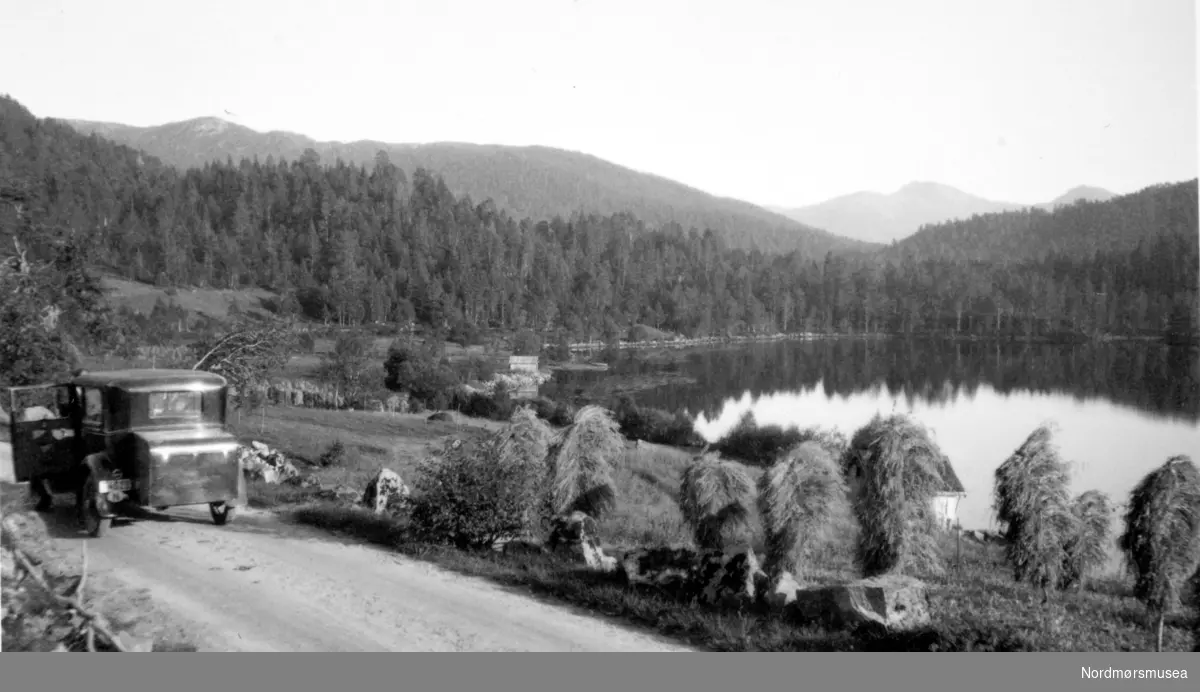 Foto av en bil langs en landevei nær skog og innsjø. Muligens i Eidsvåg, Nesset kommune? Fra Nordmøre Museum sin fotosamling. Tilleggsinfo: Dette er bilde fra Skjørsetervatnet i Nesset. Kan se bildet fra samme vinkel på Google Street view her: http://goo.gl/maps/xn6G9. (Informant: Inge Meisal.) Tilleggsinfo: Dette er på veien fra Molde over Gussiåsen til Tjelle, Rød og Eidsvåg. Vannet vi ser heter Skjørsetervannet. (Informant: Odd G. Øye.)





