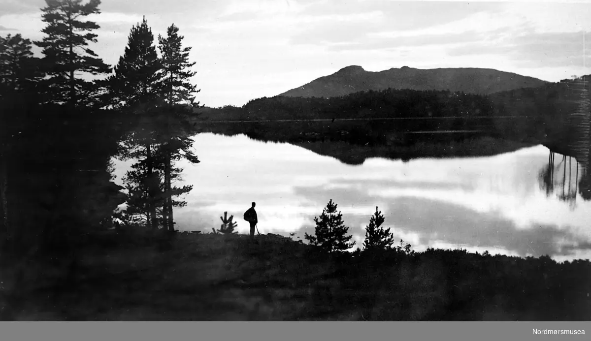 Foto fra en turgåer med sekk nede ved en innsjø usikkert hvor. Fra Nordmøre Museum sin fotosamling
