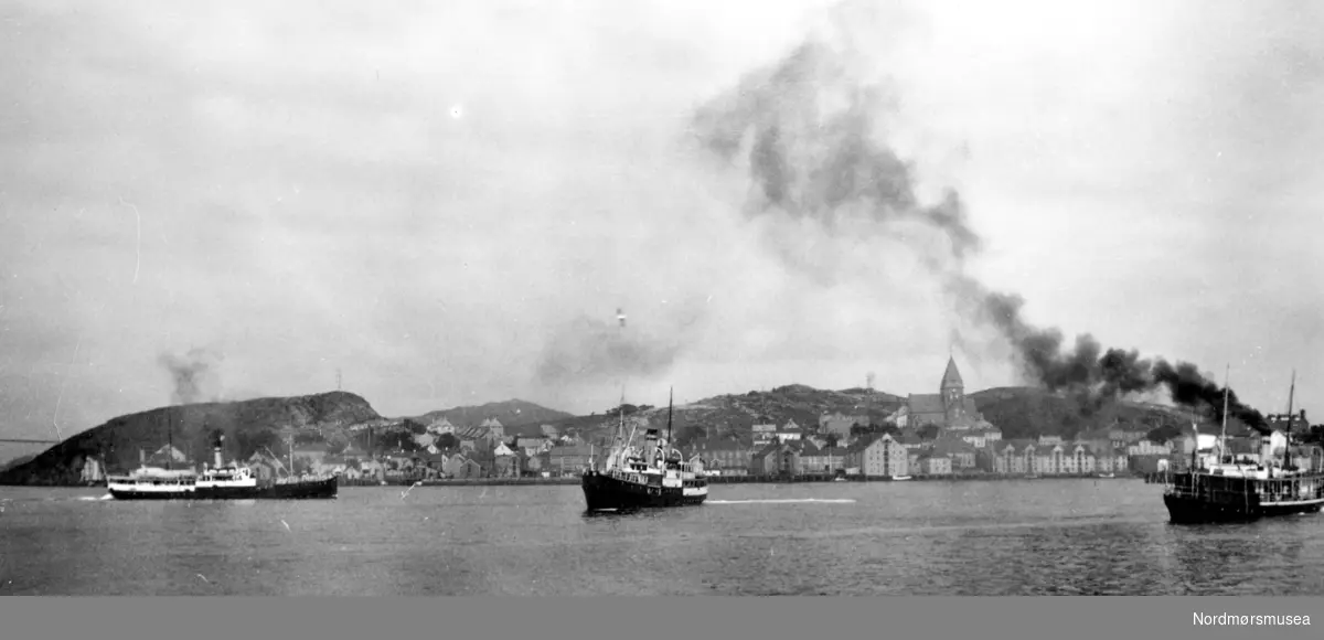 Foto fra havnebassenget i Kristiansund, hvor vi ser tre dampskip på vei inn eller ut fra havna. I bakgrunnen ser vi Nordlandet med Nordlandet kirke, som ble reist i 1914. Datering er trolig rundt 1920-1939. Fra Nordmøre Museums fotosamlinger.
