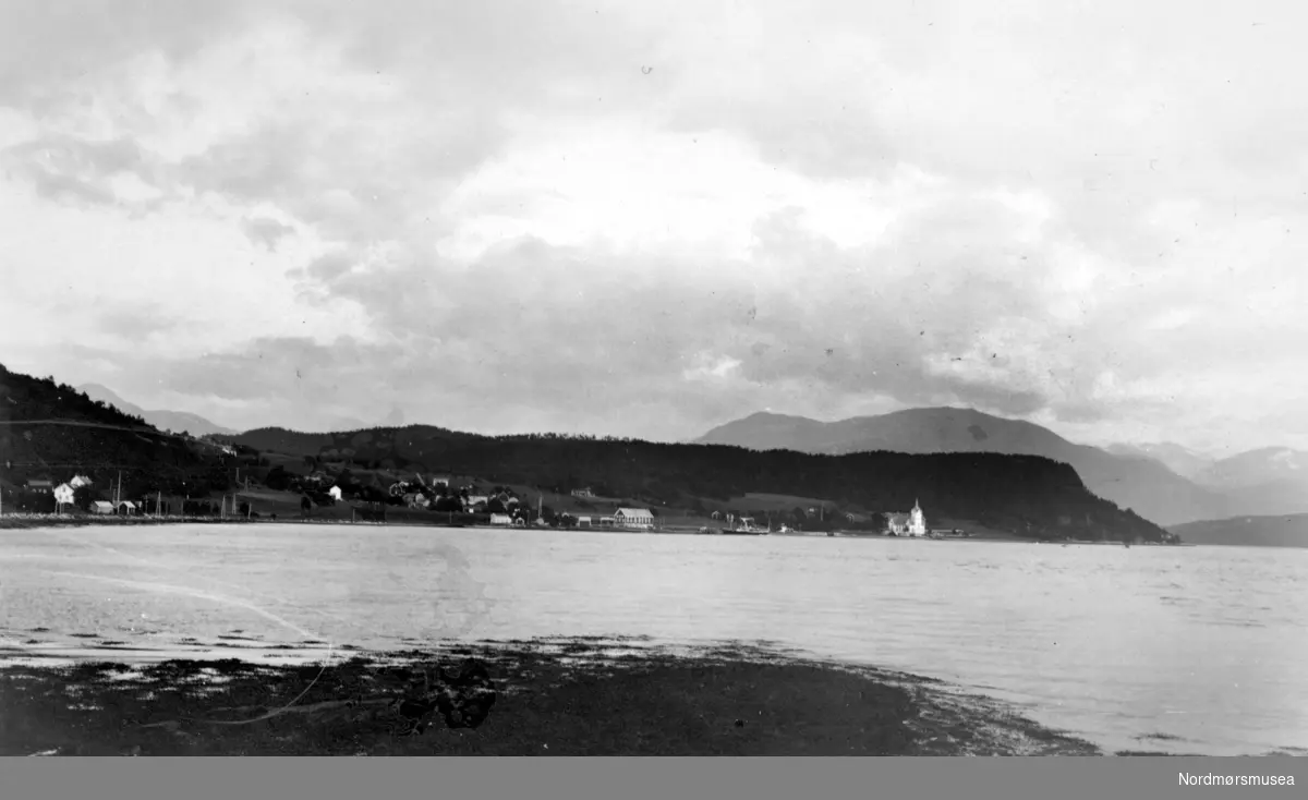 Foto fra Stangvik i Surnadal kommune, sett fra sjøsiden. Her ser vi Stangvik kirke i bakgrunnen, med andre deler av bebyggelsen. Fotograf er trolig Georg Sverdrup og bildet er svært sannsynlig datert til 1936. Se reg. nr. KMb-1987-005.3916. Fra Nordmøre Museums fotosamlinger.
