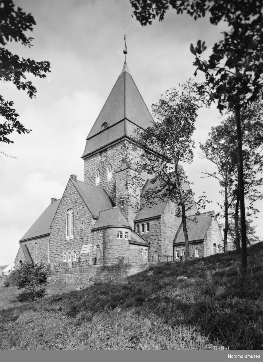 På bildet ser vi Nordlandet Kirke, som ligger på Nordlandet i Kristiansund. I 1875 besluttet bystyret i Kristiansund å bygge en kirke i denne bydelen. Det ble sikret tomt i 1883, og grunnsteinsnedleggelsen fant sted den 4. mars 1913. Nordlandet kirke ble innviet 16. desember 1914. Kirken ble tegnet av kirkearkitekt H. Schytte-Berg fra Trondheim, etter en arkitektkonkuranse mellom arkitektene H. Skytte-Berg, O. Stein og Kr. Rivertz. Rivertz står for kjente bygg i Kristiansund som Festiviteten, Norges Bank og byens nye jugenstilpregede Grand Hotell, da det første Grand Hotell brant ned i 1907. Byggmester Havnes fra Ålesund, stod for Hovedentreprisen. Mer om Nordlandet kirke kan leses her: http://kristiansund.kirken.no/tekstsider.cfm?avdelingsid=38517&amp;text_id=49401. Fra Nordmøre Museum si fotosamling. Reg: EFR

