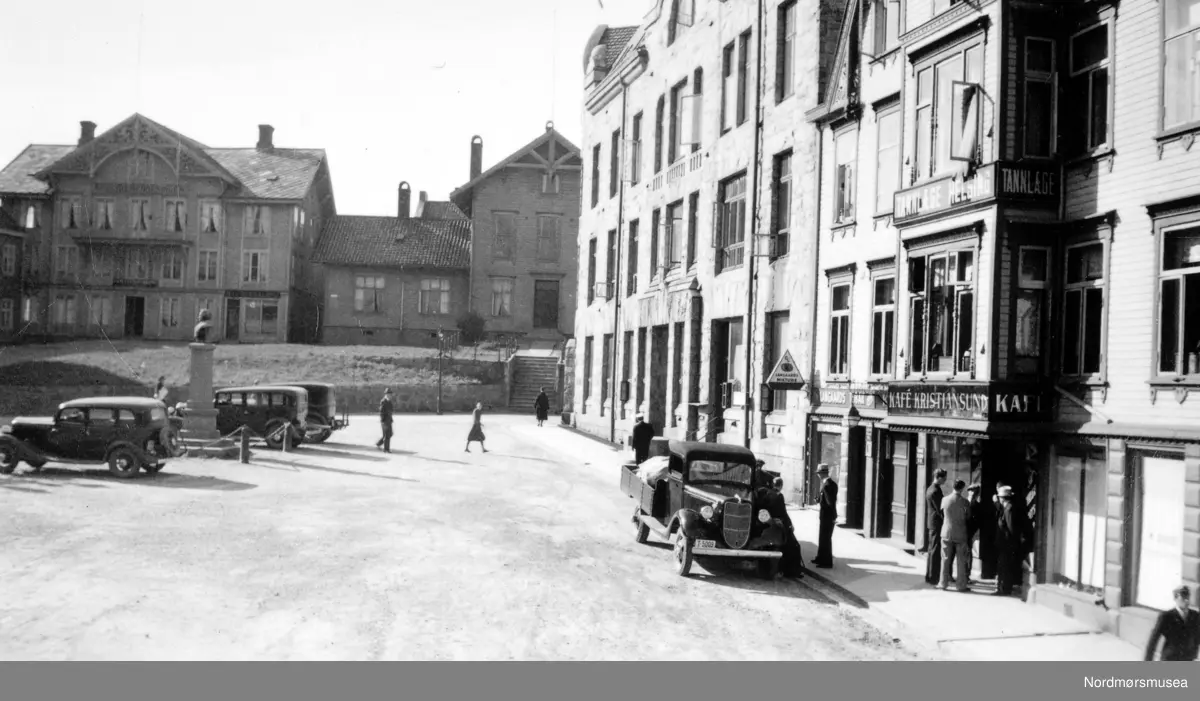 Lastebilen er en Ford V8 1936, nærmest til venstre kan være en Ford V8 1933-34 firedørs sedan. 
(Info: Ivar Erlend Stav).  - det gamle Torget på Kirkelandet i Kristiansund slik det så ut før bybrannen 28. april 1940. På bildet ser vi fra venstre Arbeider-foreningens lokaler, som også inneholdt en frisør- salong i nedre høyre del av bygget. Deretter finner vi den gamle Rådstua, mens bygget til høyre var kommunebygningen, mens i det ytterste huset helt i kanten til venstre finner vi blant annet Kafe Kristiansund og Tannlege Helsing. På torvet ser vi den kjente Christiestøtta, bysten. Denne står etter krigen i enden av president Christies gate. Fra Nordmøre museums fotosamlinger.