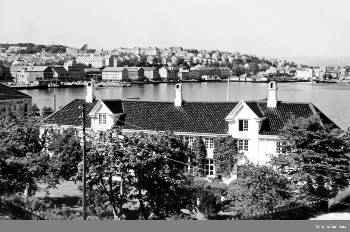 Kjøpmannsgården "Lossiusgården" fra 1780 på Innlandet i Kristiansund. I bakgrunnen sees gjenreisningsbyen og Kirklandet kirke. Gjenreisningen etter bombingen under 2. verdenskrig ble ansett som avsluttet ved oppføringen av kirken i 1964. Fra Nordmøre museums fotosamlinger. EFR2015