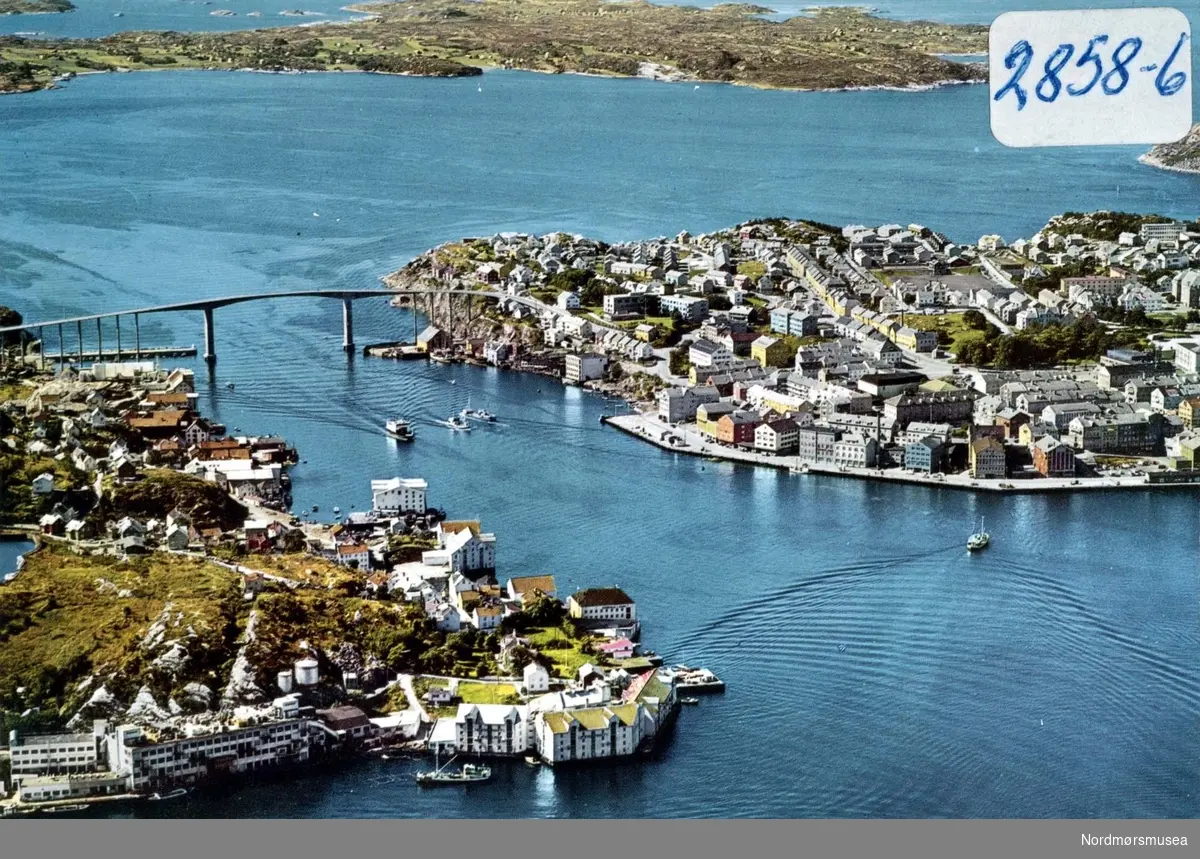 Postkort/flyfoto ";2858-6"; hvor vi ser de to landene Innlandet (til venstre) og Kirkelandet (til høyre) som er knyttet sammen over Sørsundet av Sørsundbroen i Kristiansund. Datering er ukjent, men kan muligens være fra omkring 1970 til 1975. Utgiver er usikker. Samlingen av forskjellige postkort fra Kristiansund strekker seg fra KMb-1987-005.6103 til KMb-1987-005.6161. Fra Nordmøre museums fotosamlinger. /Reg:EFR2013/
