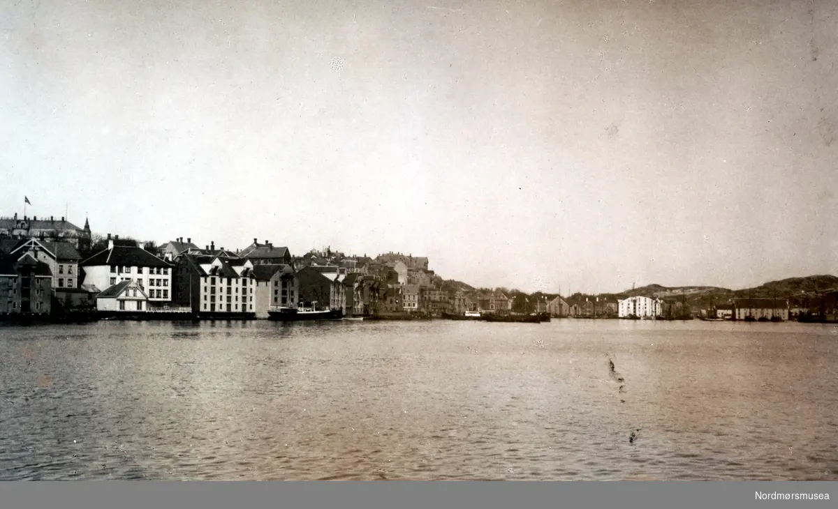 Postkort med tekst:  ";Kristiansund N.  Havnen."; Vi ser  Kirkelandet til venstre  med bebyggelsen og bryggene i Johnsenshuken og Devoldholmen i front. (Fra Nordmøre Museums fotosamlinger.)  /Reg:EFR2013/



