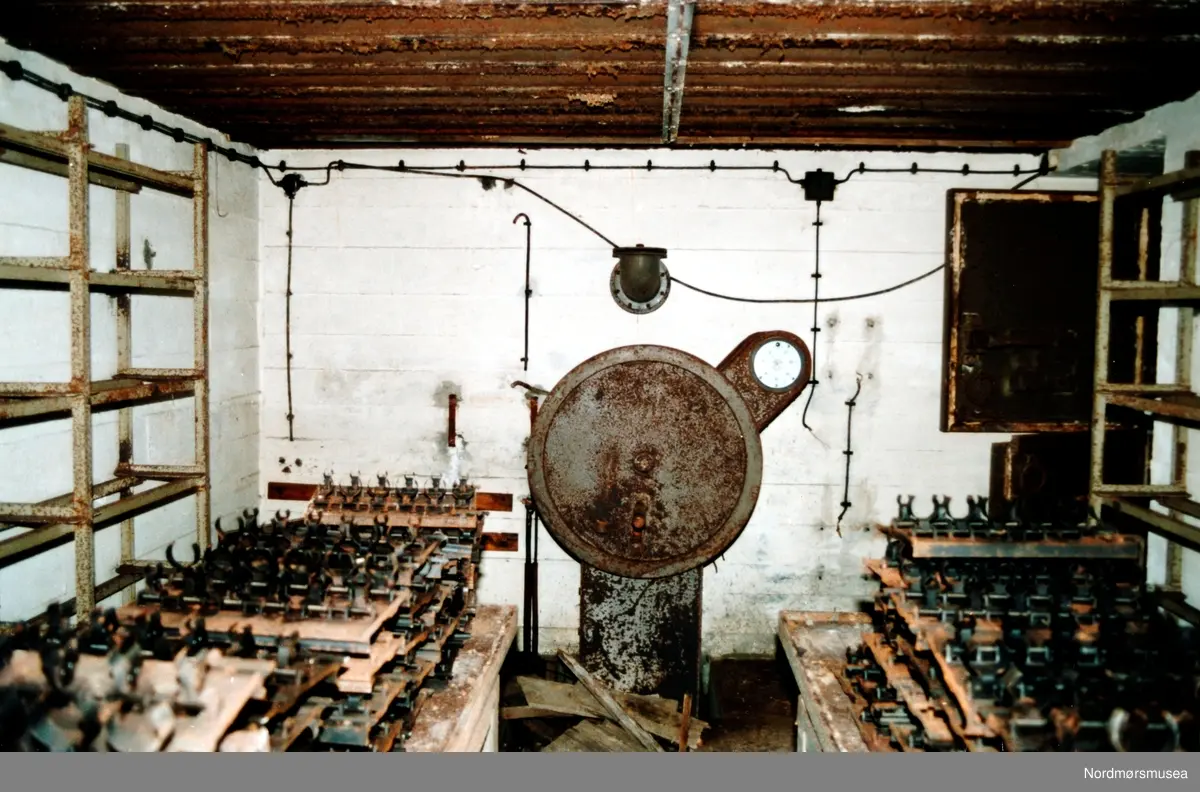 Foto fra kanonstilling i Hauggata 43 - 45 på Kirkelandet i Kristiansund. Bildet er datert 19. september 1991 og fotograf er Stein Magne Bach ved Nordmøre museum. Magasinrom 5 cm BK granater i bunker R 633. Maskinen er hånddrevet avfyring av våpensystemet hvis strømmen skulle gå.
(info: Bjørn Ove Angvik - 08.11.2016)   Se serie fra reg. nr. KMb-1991-039.0001 til KMb-1991-039.0017. Fra Nordmøre museums fotosamlinger.