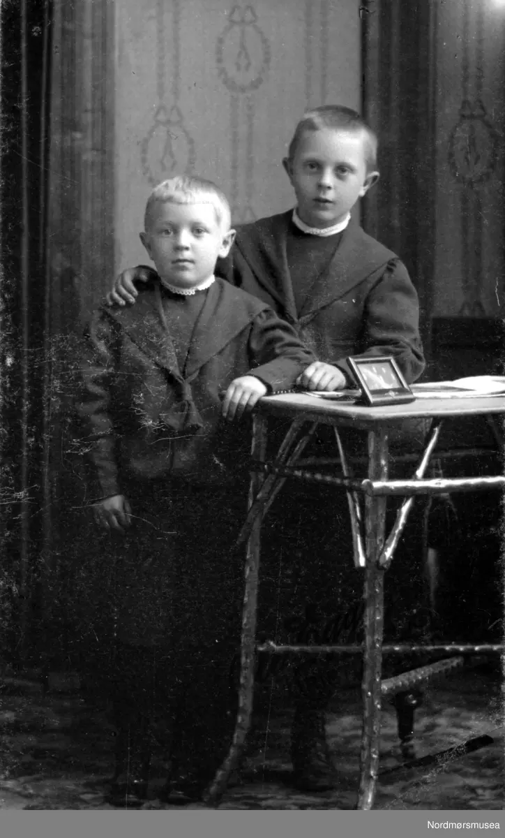 Portrett av to ukjente gutter, trolig fra Kristiansund, eller med sterk tilknytning til Nordmøre. Datering er ukjent. Fra Nordmøre Museums fotosamling. Fotograf og militærmusiker Ole Egge (1872-1956) startet i 1917 Kristiansund Guttemusikkorps med 40 gutter. Han var fotograf her 1910-30. Også gjestedirigent i Kristiansund Symfoniorkester. 17. mai 1980 ble et minnesmerke avduket foran Langveien Ungdomsskole. Født på Egge på Sjøholt i Ørskog, studier i Tyskland. Grunnla Egges mannskor 1931, flytta hjem til Sjøholt 1940.
