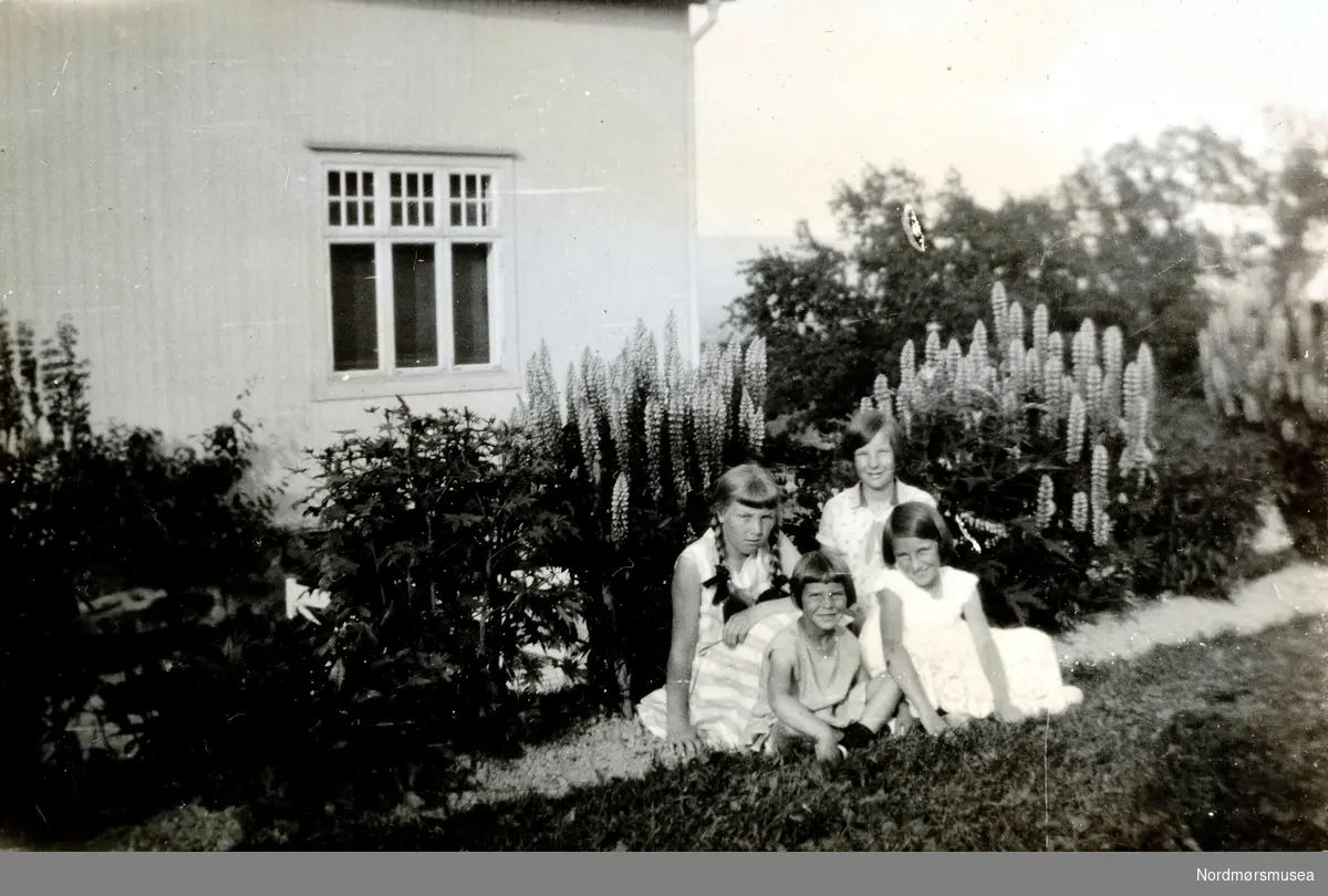 ";Firkløvret hjemme i Rælingen 1931";. foto av en gruppe barn sittende ute i hagen i Rælingen. Det er trolig barn fra Knudtzonslekten, eventuelt bekjente. Jente nr. 1 fra bakre rad til venstre (med flettene) er Christine Majorie Knudtzon g. Waagbø. Pike nummer 2 bakfra er trolig Elsa Fosse. Bildet er fra et fotoalbum fra Ida Knudtzon samlingen (serie KMb-2008-024) og strekker seg fra KMb-2008-024.0074 - KMb-2008-024.0117. Fotoalbumet har følgende påskrift ";Til lillemor fra Tante Didi. Julen 1928";. I tillegg kommer naturligvis kommentarene til hvert bilde. Fra Nordmøre museums fotosamlinger.
