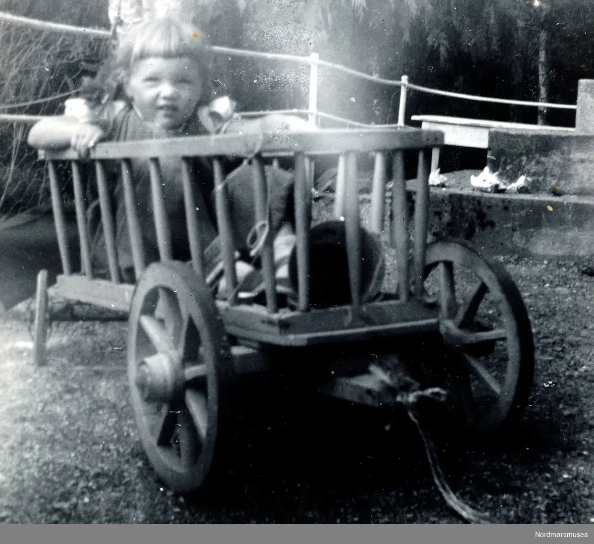 Foto fra trolig fra Fagernæs på Frei, i Kristiansund kommune, hvor vi ser Ida Margrethe Waagbø Knudtzon sittende oppe i en kjerrevogn. Trolig fra tiden rundt 1955 til 1956. Fra Ida M. Knudtzons fotosamlinger, nå en del av Nordmøre Museums fotosamlinger.

