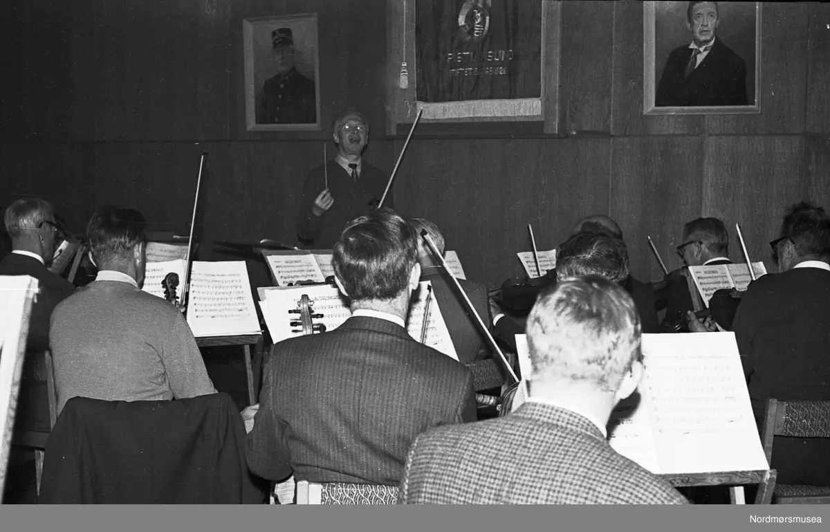 Ernst Glaser dirigerer en prøve i Tempohuset.

1967 høsten var et "lyrikk og musikk"-prosjekt med lektor Hans Kristiansen: 19.10 i Festiviteten og 20.10. på Høgtun i Torvikbukt. Både denne forestillingen og en konsert 18.11. med Liv og Ernst Glaser, datter og far som solist og dirigent i Griegs A-moll (Musikkens Venner arr.), fins på lydbånd. 17.12. medvirket KSO ved julekonserten i Kirkelandet kirke.- Notearkivet ble ryddet, Skolemusikken betalte i et anfall av dårlig samvittighet uoppfordret hundre kroner for lån av notestativer.

1968 Norsk Kulturråd slår til med 5000 kr til gjestedirigent og 5000 kr til de Premier-paukene vi fortsatt bruker. KSO måtte nemlig stadig låne pauker fra Molde, fordi våre ikke hadde stemmemekanikk. Kommunen gir 3000 til dirigentordning. - 31.januar viser NRK TV en lang reportasje fra "Byen ved storhavet", der KSO fikk 400 kr for å spille "Ut mot Havet" under Ottar Gjendems ledelse. Dette er det eldste kjente filmopptaket av orkestret. Vårkonserten var Haydns "Årstidene" i Kirkelandet kirke 31.3. Her ble det mange unødvendige runder med organist Grimsmo som hevdet at dette ikke var kirkelig musikk, og ikke huset verdig. Menighetsrådet skar gjennom og fikk Kirkedepartementets dispensasjon til å overprøve organistens vurdering, og all PR saken fikk i avisene medvirket vel til at det ble fullt hus. Og vi har lydopptak. Korsatser fra Årstidene ble gjentatt under Landbruksveka i Folkets Hus 2.4., og innbrakte kr 150. Ottar Gjendem flytter i mai til Ålesund, og Peder A. Rensvik dukker opp i hjembyen. Han leverer en privat utredning om kommunal musikkskole og foreslår 48 instrumenter innkjøpt første omgang! &ndash; 4.9. har KSO besøk fra Brighton Youth Orchestra, dir. David Gray, som holder konsert i Gymnasets Aula. Mange orkestermedlemmer som ikke kunne ta imot musikere til privat overnatting, valgte å betale hotellrom for dem på Fosna. &ndash; 10.11 dirigerer Ernst Glaser igjen. Han var i byen i 10 dager, og på programmet stod ouvertyren til "Seraillet" (som det ikke ble noe av i 1958, men som Sinfoniettaen spiller i 1999) og Schuberts femte. Her fins det to ulike lydopptak. Ottar Gjendem kom ukentlig opp fra Ålesund for å lede prøvene. En av strykeprøvene ble holdt i Speiderhytta. Peder Rensvik tiltrådte som kommunal musikkinstruktør først ved årsskiftet, men holdt sitt første møte med orkesterstyret allerede 6.12. Han foreslår 17.-mai-konsert.




ilde fra Trygve Rossbachs dokumentasjon av Kristiansund Symfoniorkesters virksomhet på andre halvdel av 1900-tallet; ca 1950-2000. Prøver, turer, sosialt samvær og konserter. (Fra Nordmøre museum sin fotosamling.)
