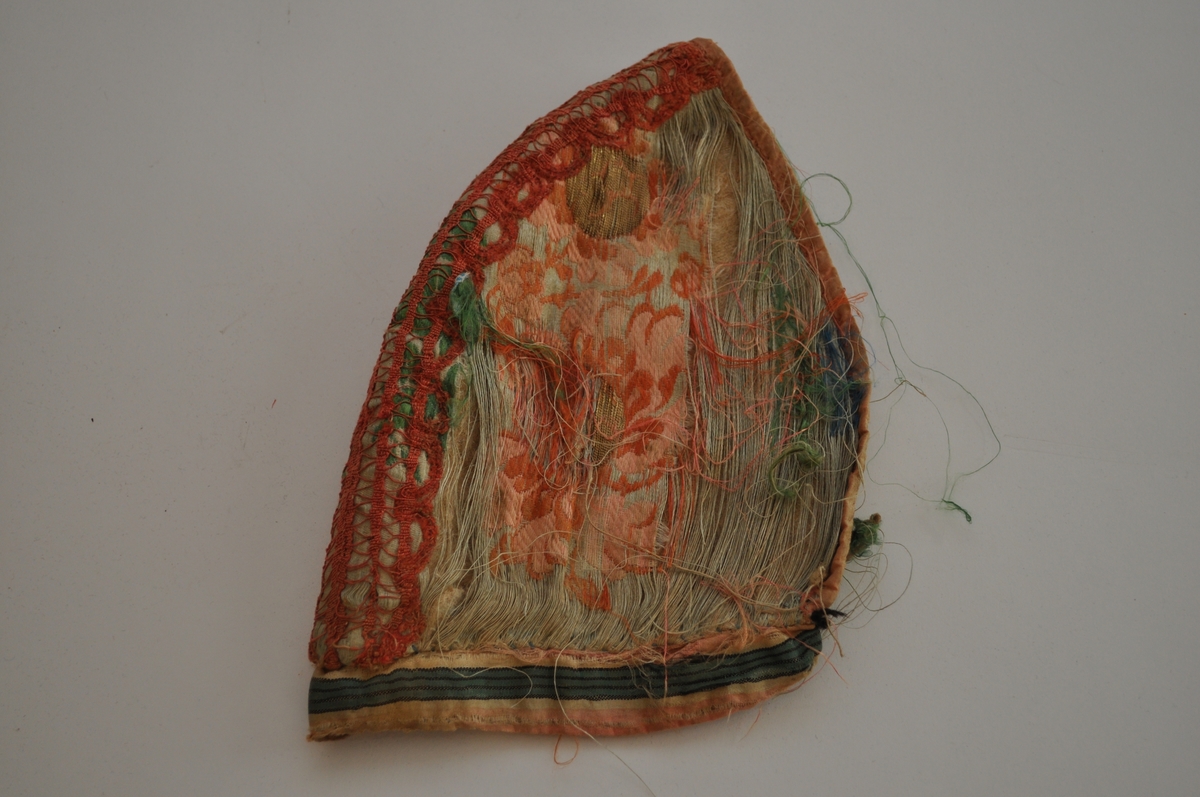 Tobladlue i lys, blågrønn silkesateng med innvevde, brosjerte blomstermotiver i lyserødt, rødbrunt, grønt og blått samt gulltråd. Stoffet kan dermed karakteriseres som brokade. Over midtsømmen løper en lakserød blonde og langs nederkanten er et stripet silkeband i lyserødt, hvitt, grønt og svart. Framkanten er kantet med et lyserødt silkeband. Fôret er av ubleiket linlerret. Lua er sydd sammen med silketråd i hvitt, blått og lyserødt. Silkestoffet er brustent, så lua framstår som den er har dårlig tilstand.