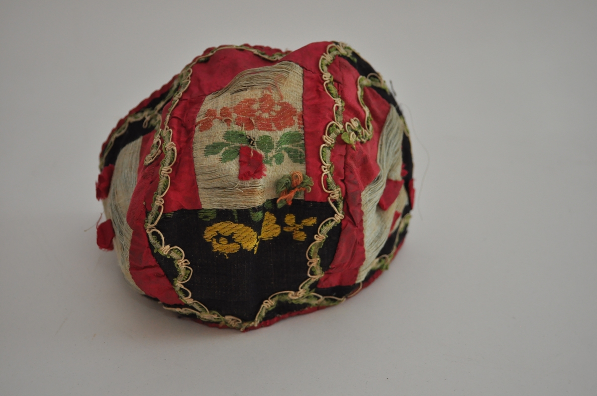 Lua er ei trebladlue med to speilvendte sidestykker og et tilnærmet rektangulært midtstykke. Hovedstoffene er av silke, sydd sammen av 15 biter. Tre biter er av lys, blågrøn silke, hvorav en bit har brosjert blomster- og bladmotiv. Fem biter er svarte, hvorav en bit har brosjert mønster i gult og grønt. Sju biter er av cerisse-rød silke, hvorav minst to er av damask. Langs kantene, sømmene og øverst på sidestykkene er lua dekorert med en blonde av hvit og grønn silketråd. På hvert sidestykke er fem små cerisse-røde silkebiter sydd fast. Ytterligere en er sydd på midtstykket bak, og det er rester etter minst en til samme sted. I skjøten mellom tre stoffbiter på midtstykket bak er det sydd på en trådrosett av lyserød og grønn silketråd, av samme materiale og type som på henglene registrert som OT.5342 AB. Lua er fôret med ubleiket linlerret, stykkene er sydd sammen og sårkantene kastet over til hver side, synlig på vranga. Framkant og nederkant er dekket av cerisse-rød silke, sydde til med lyseblå silketråd. Det er trådspor etter knyteband i lua.