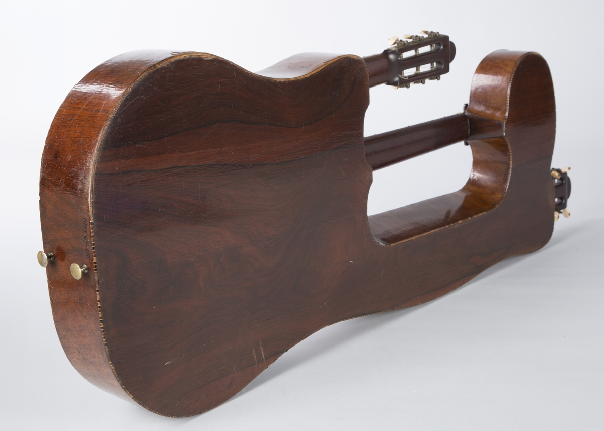 Trippelgitar, 3 halser. Lokk av gran, består av 3 deler, bunn og sarg muligens en sort mahogny. Den lengste halsen fortsetter øverst ut i en ny resonanskasse, hvis overside tjener som skruekasse for den mellomste halsen. Her er også et lydhull. En ekstra resonanseffekt oppstår ved at strengene som løper over denne resonanskassedelen under spillet svinger med. Instrumentet er utsmykket med rike perlemosrsforsiringer, delvis stekt fargede. Ornamentene er dels svært enkle og dels meget delikate blomstermønstre. Hovedlydhullet er omgitt av en 4 cm. bred krans av geometrisk intarsia, som kan minne om maurisk stil. Instrumentet har i alt 4 lydhull og 3 adskilte strengestoler. Den lengste halsen har 7 frittsvingende bass-strenger de to andre hver 6 strenger og 13 tverrbånd av metall. Runde skruehoder av elfenben. Likeså oversadler og strengestoler av elfenben.
Usignert.