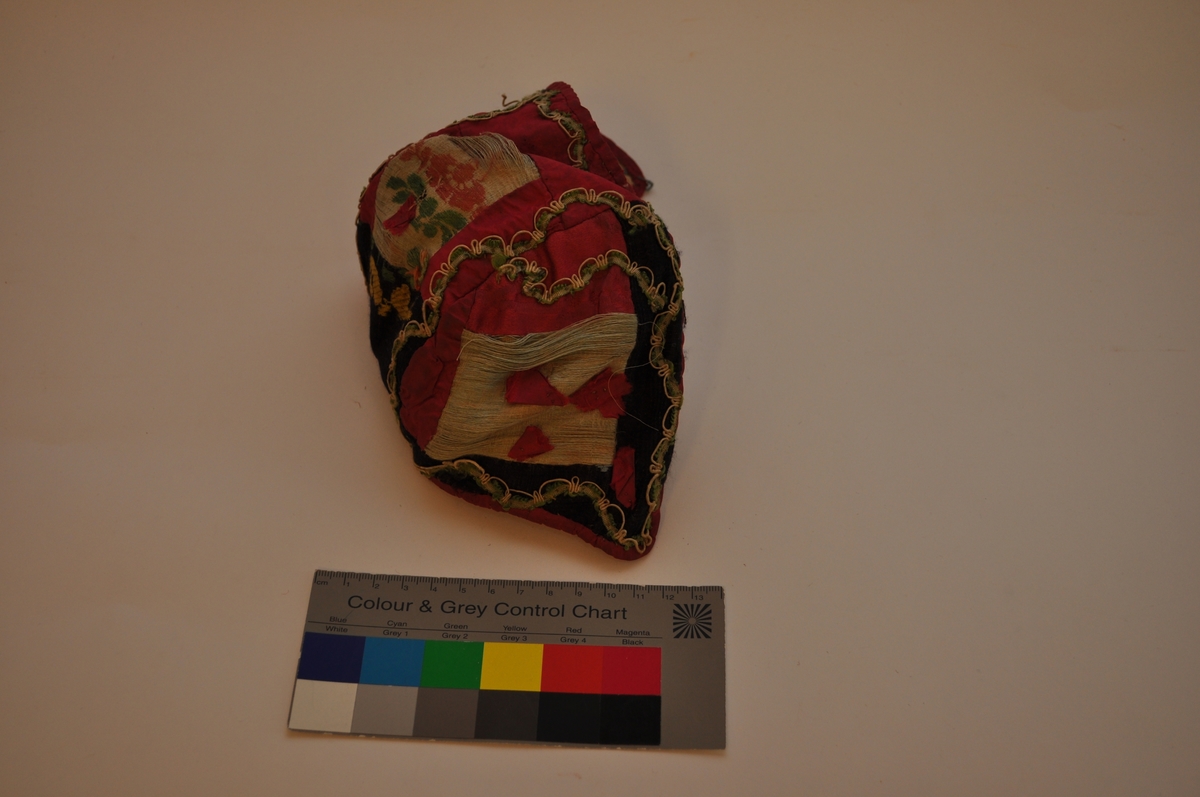 Lua er ei trebladlue med to speilvendte sidestykker og et tilnærmet rektangulært midtstykke. Hovedstoffene er av silke, sydd sammen av 15 biter. Tre biter er av lys, blågrøn silke, hvorav en bit har brosjert blomster- og bladmotiv. Fem biter er svarte, hvorav en bit har brosjert mønster i gult og grønt. Sju biter er av cerisse-rød silke, hvorav minst to er av damask. Langs kantene, sømmene og øverst på sidestykkene er lua dekorert med en blonde av hvit og grønn silketråd. På hvert sidestykke er fem små cerisse-røde silkebiter sydd fast. Ytterligere en er sydd på midtstykket bak, og det er rester etter minst en til samme sted. I skjøten mellom tre stoffbiter på midtstykket bak er det sydd på en trådrosett av lyserød og grønn silketråd, av samme materiale og type som på henglene registrert som OT.5342 AB. Lua er fôret med ubleiket linlerret, stykkene er sydd sammen og sårkantene kastet over til hver side, synlig på vranga. Framkant og nederkant er dekket av cerisse-rød silke, sydde til med lyseblå silketråd. Det er trådspor etter knyteband i lua.