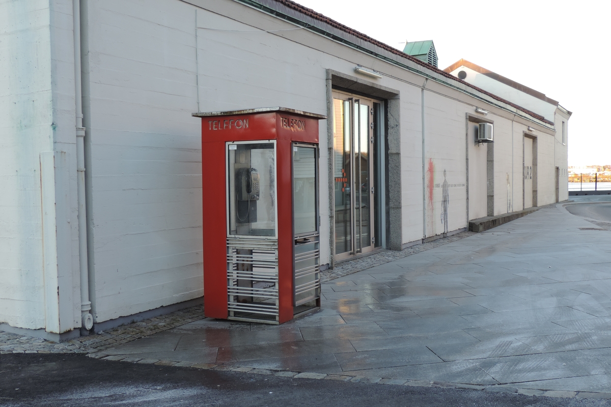 This is the story of how Norway’s most important conversation-space was designed by a young, freshly graduated man from Bergen.

“Norwegian architects are hereby invited…”
In the autumn of 1932, Oslo Telefonanlegginitiated an architectural competition. Finally, Oslo would get its own telephone booth. The city had had so called “talking-stations” from 1885, which in turn were overtaken by automatic telephones 
 only available at selected Narvesen kiosks. The state 
was of the opinion that now was the time to offer the public a better service; public telephone booths open 24/7, like the ones they already had in Sweden and England. But what would they look like, these new telephone booths? What considerations would it
 be necessary to take when designing it? The telegraph board developed a detailed list of demands and restraints: “The booth is intended to be placed outside on the streets and squares and need to be designed so that snow and ice does not hinder the opening and closing of the doors,” they wrote. “To prevent vandalism, theft, uncleanliness etc. inside the booth, it needs to be designed so that from all angles one may see what is going on in there.” Additionally, it would need to withstand storms and bad weather, and “preferably also being whipped by rain mixed with seawater” 

This was not all: The appearance would have to be «pleasing». The booth also needed to be movable, so that it could be taken in to be serviced at Telegrafverket’s main workshops. The reqired material was iron, and the surface was to be spray painted  preferably using car-body paint. There was a requirement for “a writing shelf, a pack shelf, and a suitable place for the telephone catalogue.” Also, there would need to be an illuminated TELEFON  sign, easily visible from all four angles. The total cost for each booth should not exceed 1000 kroner. The first prize for coming up with such a product was 800 kroner.

“Norwegianarchitects are hereby invited to partake in a competition for the design of a telephone booth…”  

The man with the solution
«At some point in 1932, Georg Fredrik sat at a party in Bergen. Maybe he felt a bit lost and forgotten as he often had throughout his life. He retreated to a quiet corner, took out a pencil and strted doodling on a matchbox.  According to my mother, this was how the telephone booth came into being.” In the book “Norges lille røde  historien om telefonkiosken,” Lars Fasting describes his father, the man who is far less known than the iconic architctural structure he left behind. Georg Fredrik Fasting was from Bergen, born into a family of working people and smallholders. One unusual facet of Georg Fredrik was that he was born without ears. His mother made sure he learnt to speak, read and write, 
ut Lars Fasting indicates that his father would seek refuge in drawing when the social challenges became too much to bear. And in the end drawing became his profession. In 1924 he secured a guarantor for a student loan, and started studying to become an a
rchitect at the NTH. Throughout the 1930s he entered several architectural competitions, with drafts produced, according to his son, “after work and in the late hours of the night.”

His efforts were not wasted. Out of 93 entries, with names such as “Flirt”, “Brrr”, “Ring” and “Amor”, the jury selected Fasting’s submission, “RIKS” as the new telephone booth: “The draft shows a strikingly simple solution to the task, technically as well as aesthetically well worked out.”

Taut and provident
Simple and aesthetc are the keywords here. Fasting had designed a booth pointing towards the future, and to modernism. Just how modern it was can be seen by comparing RIKS to the British telephone booth, also designed in the interwar-era. While the British version with it classicistic style is looking back to the heyday of the empire, Fasting’s booth is progressive and functionalistic. Like most Norwegian architects, Fasting broke with the classicistic style of architecture after the Stockholm-exhibition in 1930. “After it, almost all buildings erected in Norway until the German invasion in 1940, were in the functionalistic architectural style,” writes senior curator of architecture at the Norwegian National Museum, Ulf Grønvold, in the book, “Den lille røde”.“TheNorwegian booth is a piece of functionalistic architecture, an asymmetric composition with its roof slab overhanging the word TELEFON, in bold sans seraph lettering,”concludes Ulf Grønvold.

Fashionably red
And it was red. Fasting chose a colour which was part of the modern palette. “A bright red colour, but not as shiny as a signal red, the character of the colour places it among the fashionable colours within functionalism,” states paintings conservator and researcher in NIKU (Norwegian Institute for Cultural Heitage Research), Jon Brænne. In his opinion, Fasting went for visibility without making the booth stand out too much from its surroundings. The original colour was in use up to around 1950, when it changed to signal red. Towards the end of the 1970s the clour was again adjusted towards today’s orangey red.

The design, however, has not changed. RIKS is eighty years and still looks remarkably good. That’s what makes Fasting’s telephone booth a classic  even before it was added to DOCOMOMO’s list over moden icons of design. For Telenor, the telephone booth has served as a pathway into the hearts of the public. For many, Telenor (Televerket) was synonymous with exactly this telephone booth, because this was where one would go to place a call. Having a home
phone was not common until the 1980s. As such the red box became part of the Norwegian everyday and consciousness. The symbol- and publicity value of this is hard to evaluate, but in 2007 it was time to give honour where honour was due, Telenor, in consul
tation with the Directorate for Cultural Heritage, decided to preserve 100 telephone booths for all eternity.

And what about Georg Fredrik Fasting? What happened to him? At the age of 56 an entry in his diary states: «I CAN HEAR». As the first person in th world he had undergone an operation where he had ear canals constructed and eardrums fitted. For the rest of his life, the man behind Norway’s own telephone booth could answer the telephone himself.

Source: Norges lille røde historien om telefonkiosken (2007), issued by The Norwegian Telecom Museum and Telenor Cultural Heritage.