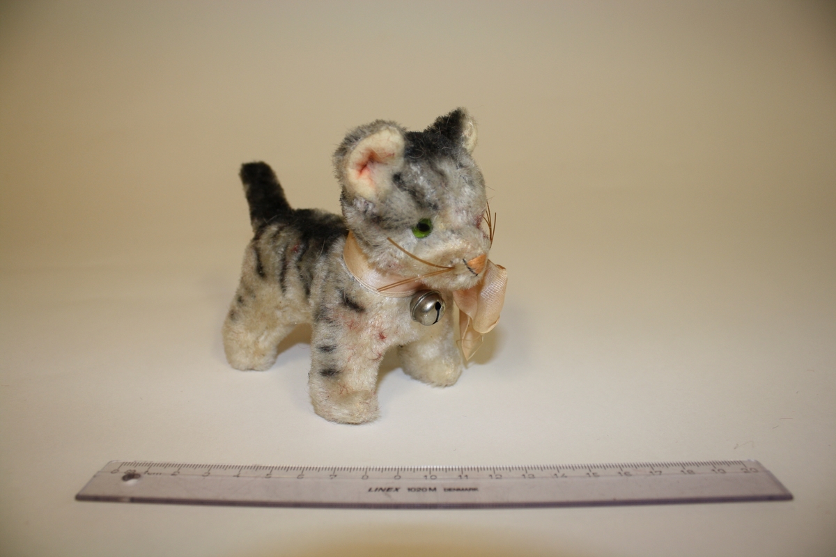 Gitt av Lisbeth Andreassen Chumak. Gråstripete katt med bjelle og rosa sløyfe. Fra 1950 tallet.