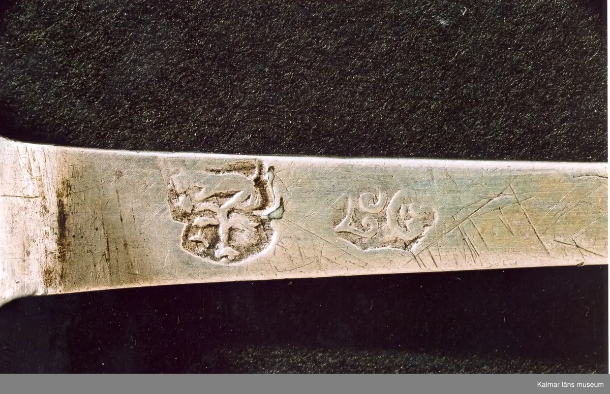 KLM 3010. Sked. Av silver. Renässanstyp kerubsked, med runt blad, kort, platt skaft slutande med en kerubknopp. Blad med graverad dekor, en blomma. Stämplar: stadsstämpel Vimmerby; mästarstämpel L.C. för Lars Castman 1739-1784; årsstämpel saknas.