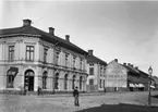 Drottninggatan österut från Järnvägsgatan ca år 1900. Hörnhuset uppfördes 1877, byggdes på med 2 våningar 1904 och ytterligare en 1955 till dagens utseende.