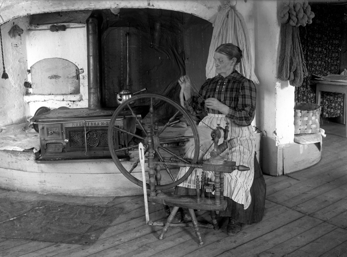 Frammegården i Skillingmark. Donerades till hembygdsföreningen 1941 av fröken Kerstin Eriksson som var den sista fast boende på gården. Gården är ett av Sveriges mest omtalade spökhus.
Fotot föreställer Karin Holm. Hon sitter i köket på sin gård och spinner. Hon bodde på gården Västsuga i Holmserud Skillingmark. Huset är numera riven men var liknande Frammegården. 