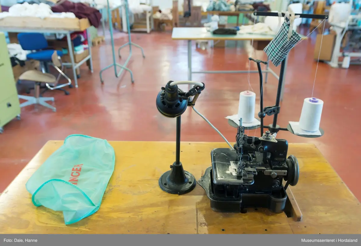 Ei to-tråds Singer symaskin til falding/kantar på strikka stoff, med original motor, lampe, montert på bord. 

Modell 81-6, merka med nummer 54. Maskinnummer AB503010. Overlockmaskin med faldeapparat, til kanting av stoff.