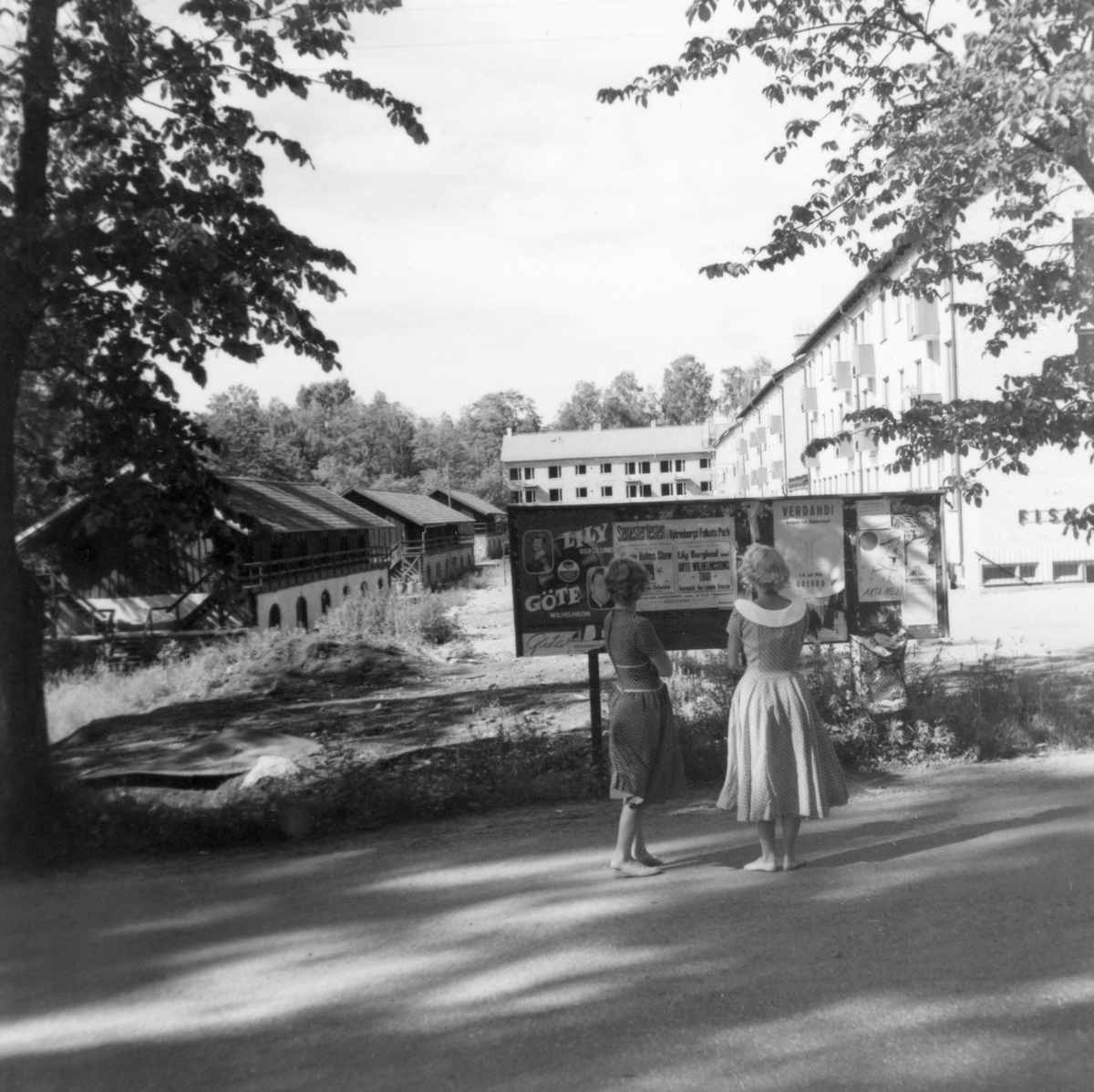 Någonstans i Värmland - från sluet av 1950-talet. Kommentar från en användare:"När man zoomar in texten på anslagstavlan så står det att det är dans i Björneborg. Bilden är troligen från Björneborg". Nytt citat: "Det är Björneborg. Såväl uthusen som hyreshusen finns kvar idag. Flickorna står på Degerforsvägen och bilden är tagen mot norr".