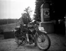 En kvinna på motorcykel, registreringsnr: T1642. 
Motorcykeln är en Harley-Davidson som registrerades den 20:e december 1922 och ägdes av Valfrid Larsson, Sirbo, Nysunds socken.