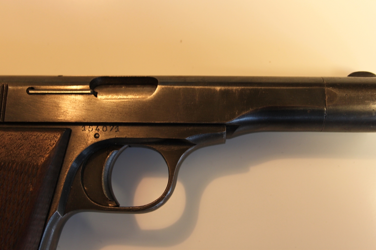 Brunt deksel på hver side av pistolskaftet. Med «Rutemønster». Festet med gjennomgående skrue. Magasin sitter i.