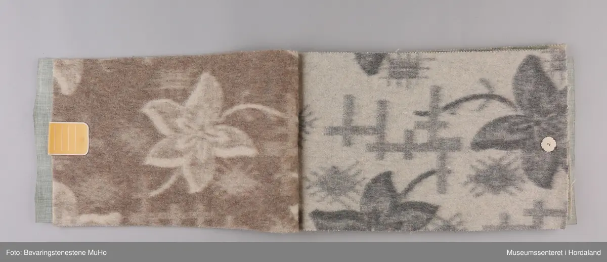 Stoffprøvebok frå Salhus Væverier. Prøver på ullteppe med blomstermotiv, feste i papp/hyssing. Omslag i grønt plastbelagt stoff i skinnimitasjon/skai.