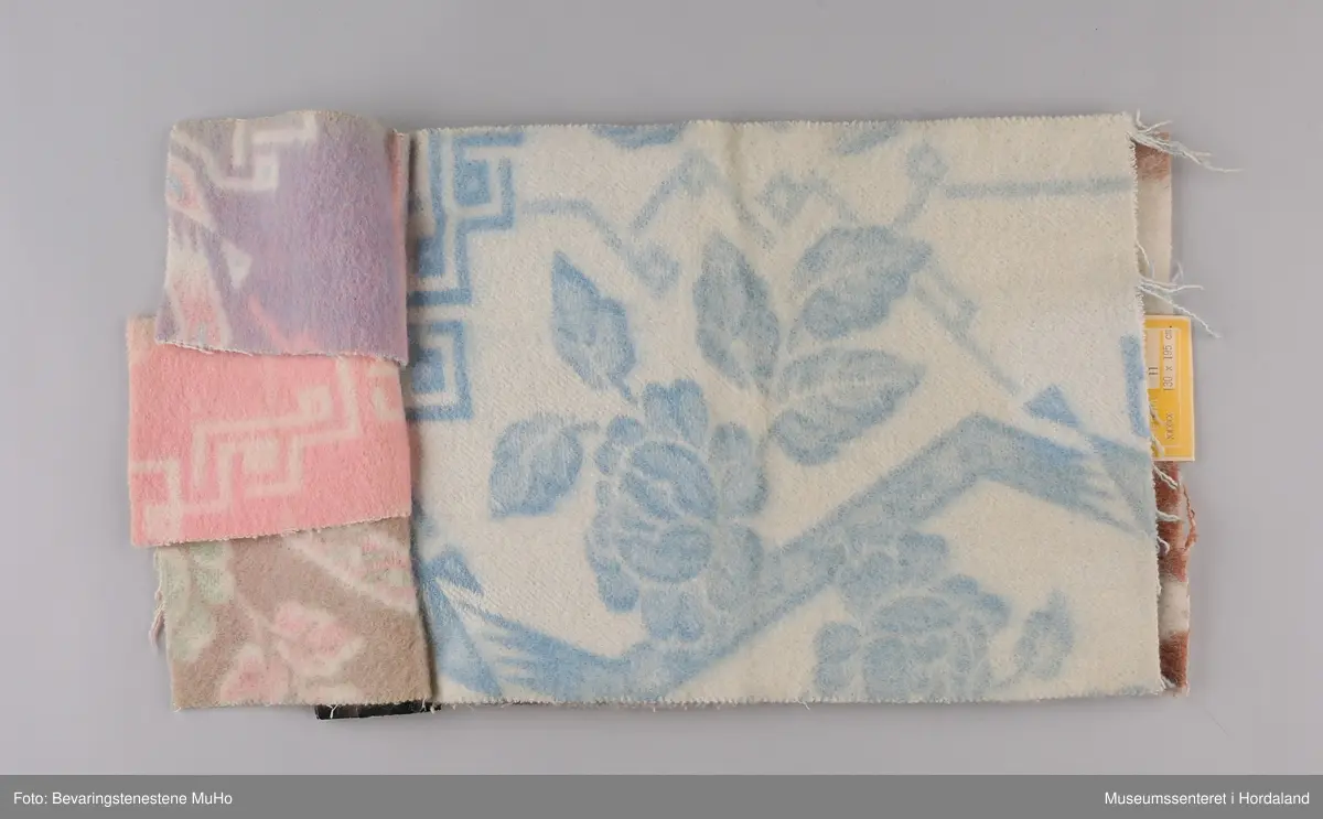 Stoffprøvebok frå Salhus Væverier. Prøver på ullteppe i to fargar, med blomstermønster. Feste i papp.