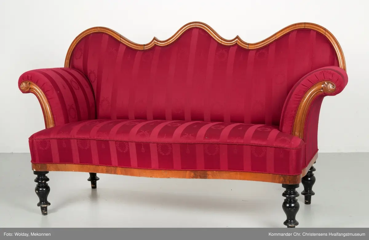 Akantusdekor i treverket. Dekor m/possementsnorer. Baksiden av sofaen er laget av et billigere treslag, der det ikke synes. Sofaen er nok ment å stå inntil en vegg. Grønt stoff ble brukt som underlag før det røde.