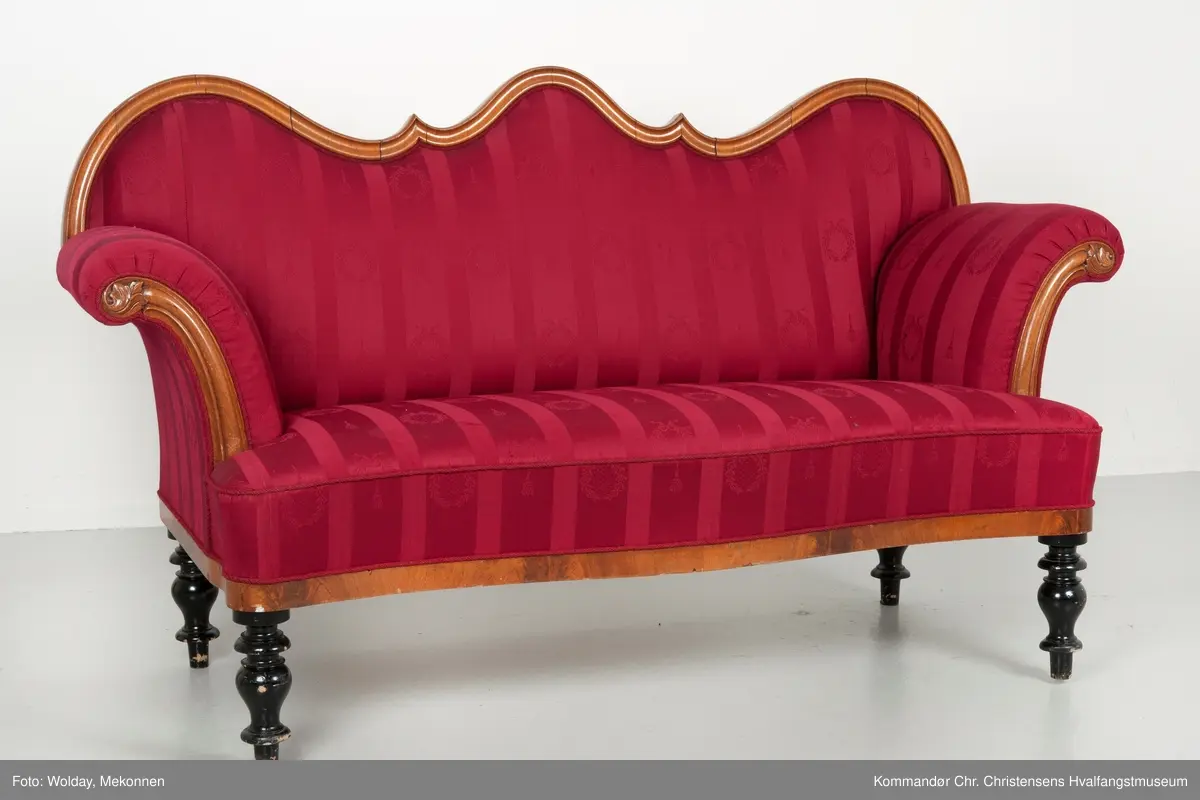 Akantusdekor i treverket. Dekor m/possementsnorer. Baksiden av sofaen er laget av et billigere treslag, der det ikke synes. Sofaen er nok ment å stå inntil en vegg. Grønt stoff ble brukt som underlag før det røde.