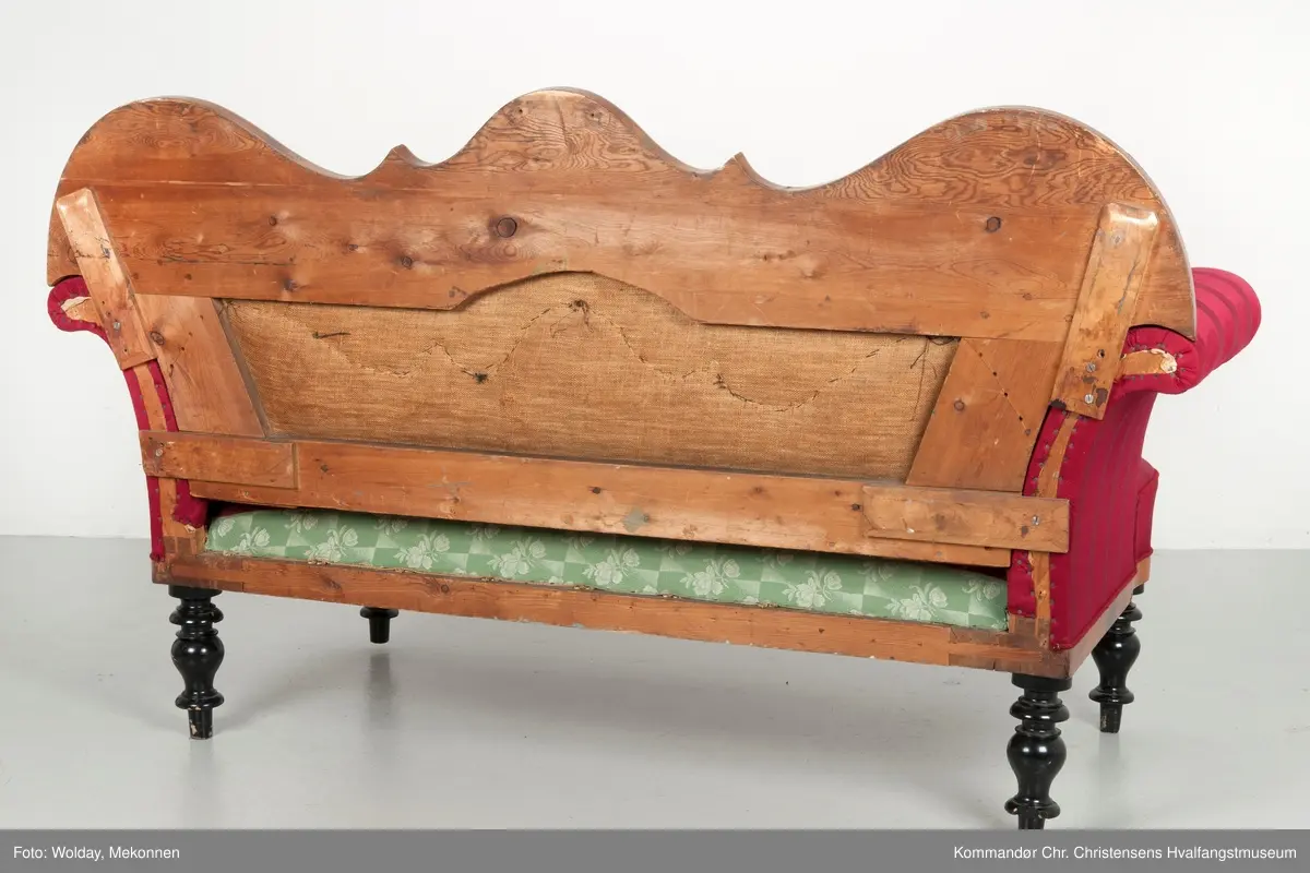 Akantusdekor i treverket. Dekor m/possementsnorer. Baksiden av sofaen er laget av et billigere treslag, der det ikke synes. Sofaen er nok ment å stå inntil en vegg. Grønt stoff ble brukt som underlag før det røde.