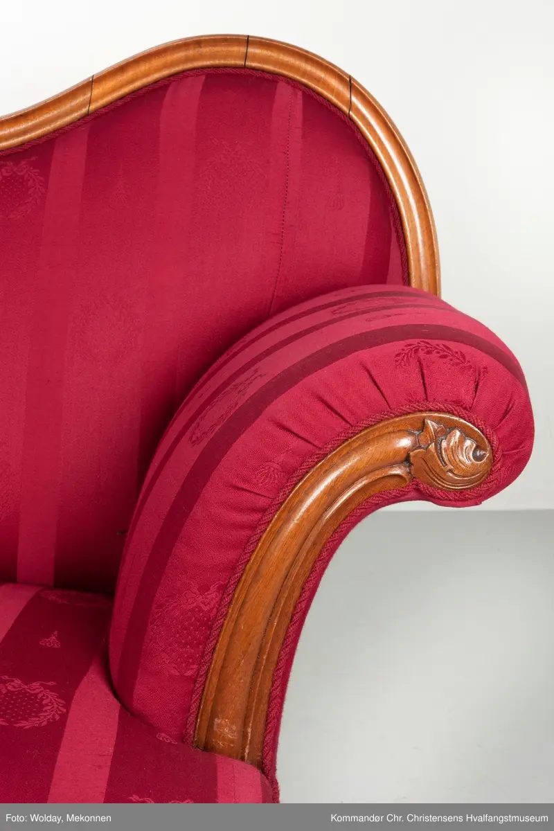 Akantusdekor i treverket. Dekor m/possementsnorer. Baksiden av sofaen er laget av et billigere treslag, der det ikke synes. Sofaen er nok ment å stå inntil en vegg. Grønt stoff ble brukt som underlag før det røde.