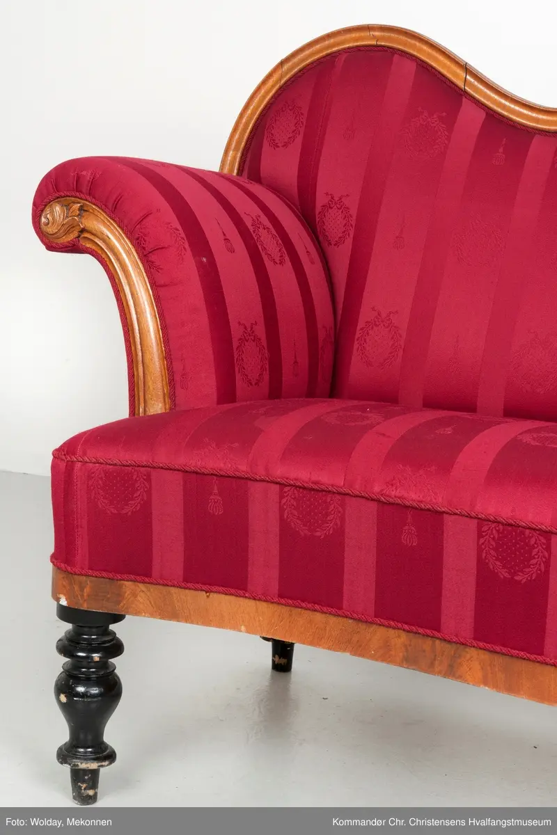 Akantusdekor i treverket. Dekor m/possementsnorer. Baksiden av sofaen er laget av et billigere treslag, der det ikke synes. Sofaen er nok ment å stå inntil en vegg. Grønt stoff ble brukt som underlag før det røde.