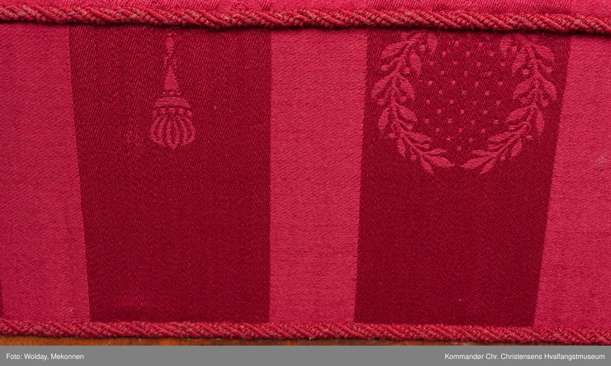 Akantusdekor i treverket. Dekor m/possementsnorer. Baksiden av sofaen er laget av et billigere treslag, der det ikke synes. Sofaen er nok ment å stå inntil en vegg. Grønt stoff ble brukt som underlag før det røde.