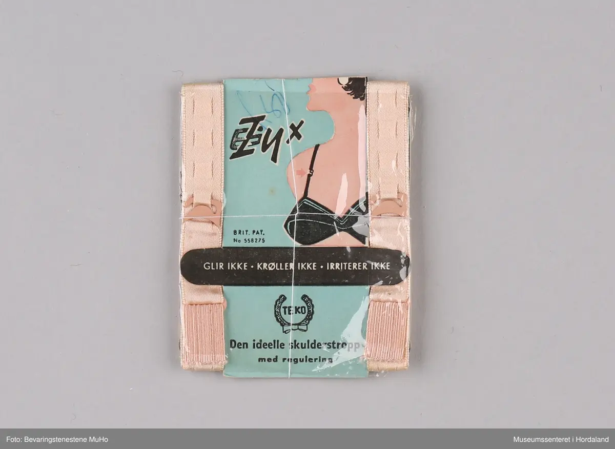 Ferskenfarga "Tyx" skulderstropper til BH, i tekstil og elastikk med metallhekter. Norskprodusert av Teko fabrikker i Bergen, pakka i papp- og plastemballasje.