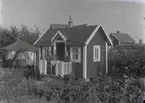 En stuga, man och kvinna i Kalmar södra koloniområde, fotograferat omkring 1930. Kalmar södra koloniförening grundades 1917 och har idag 105 kolonilotter. Området ligger strax söder om länssjukhuset i Kalmar med huvudingång från Stensbergsvägen.