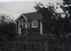 En stuga, man och kvinna i Kalmar södra koloniområde, fotograferat omkring 1930. Kalmar södra koloniförening grundades 1917 och har idag 105 kolonilotter. Området ligger strax söder om länssjukhuset i Kalmar med huvudingång från Stensbergsvägen.