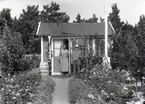 En man och en kvinna vid en liten stuga i Kalmar södra koloniområde, fotograferat omkring 1930. Kalmar södra koloniförening grundades 1917 och har idag 105 kolonilotter. Området ligger strax söder om länssjukhuset i Kalmar med huvudingång från Stensbergsvägen.