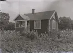 En stuga, två kvinnor och ett barn i Kalmar södra koloniområde, fotograferat omkring 1930. Kalmar södra koloniförening grundades 1917 och har idag 105 kolonilotter. Området ligger strax söder om länssjukhuset i Kalmar med huvudingång från Stensbergsvägen.