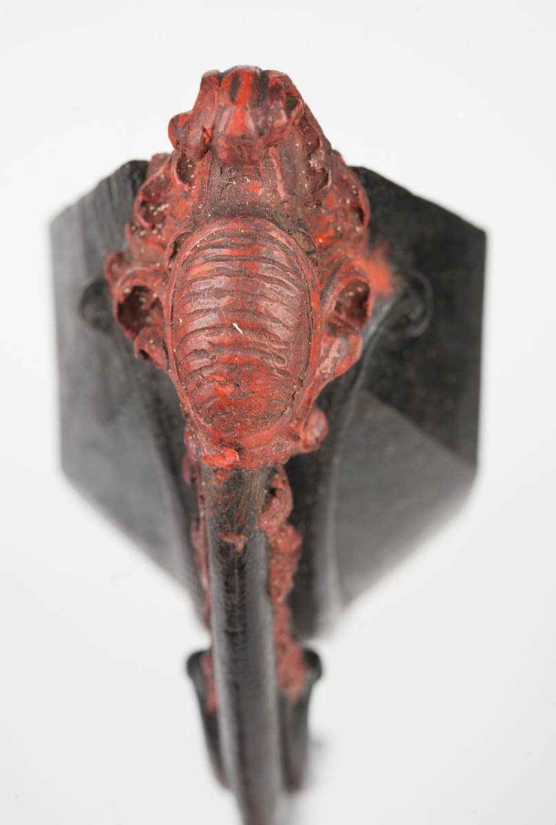 Okänt fartyg. Vapensköld med räfflad botten, krönt av volut och omgiven av blad och bladslingor. Monterad till stävkonstruktion av svartmålat trä. Bottenplattan saknas. Röd vax.