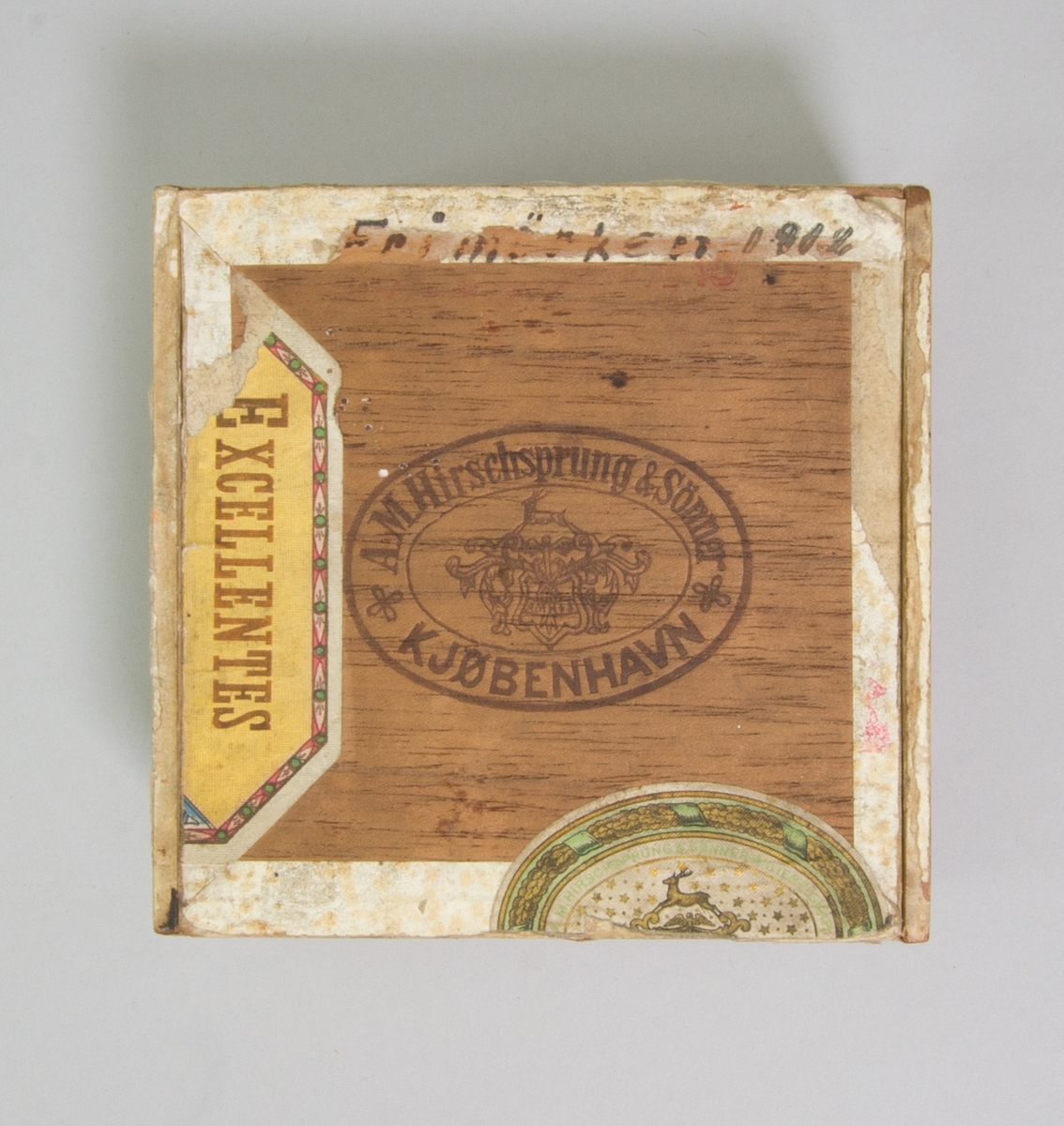 Sydonsask, fd cigarrlåda, av trä kvadratisk med fällock. Innehåller bland annat en rulle med gul tråd, en del av en tändsticksask omlindad med svart tråd, en del av en tändsticksask omlindad med beige tråd och två synålar samt trasig lornjett med guldfärgade bågar. På lockets insida påklistrat frimärke 10 öre med Gustav V:s bild, rött.