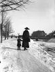 Här ses Ingeborg Malmberg, född Olsson, tillsammans med Ingrid Brundin, ca 1915-1916. I bakgrunden syns Dalapalatset och Svängbron. Snön från Gävles gator och gårdar kördes med häst och släde och stjälptes ut i Gavleån, så man kunde gå över ån på snövallarna vissa år.