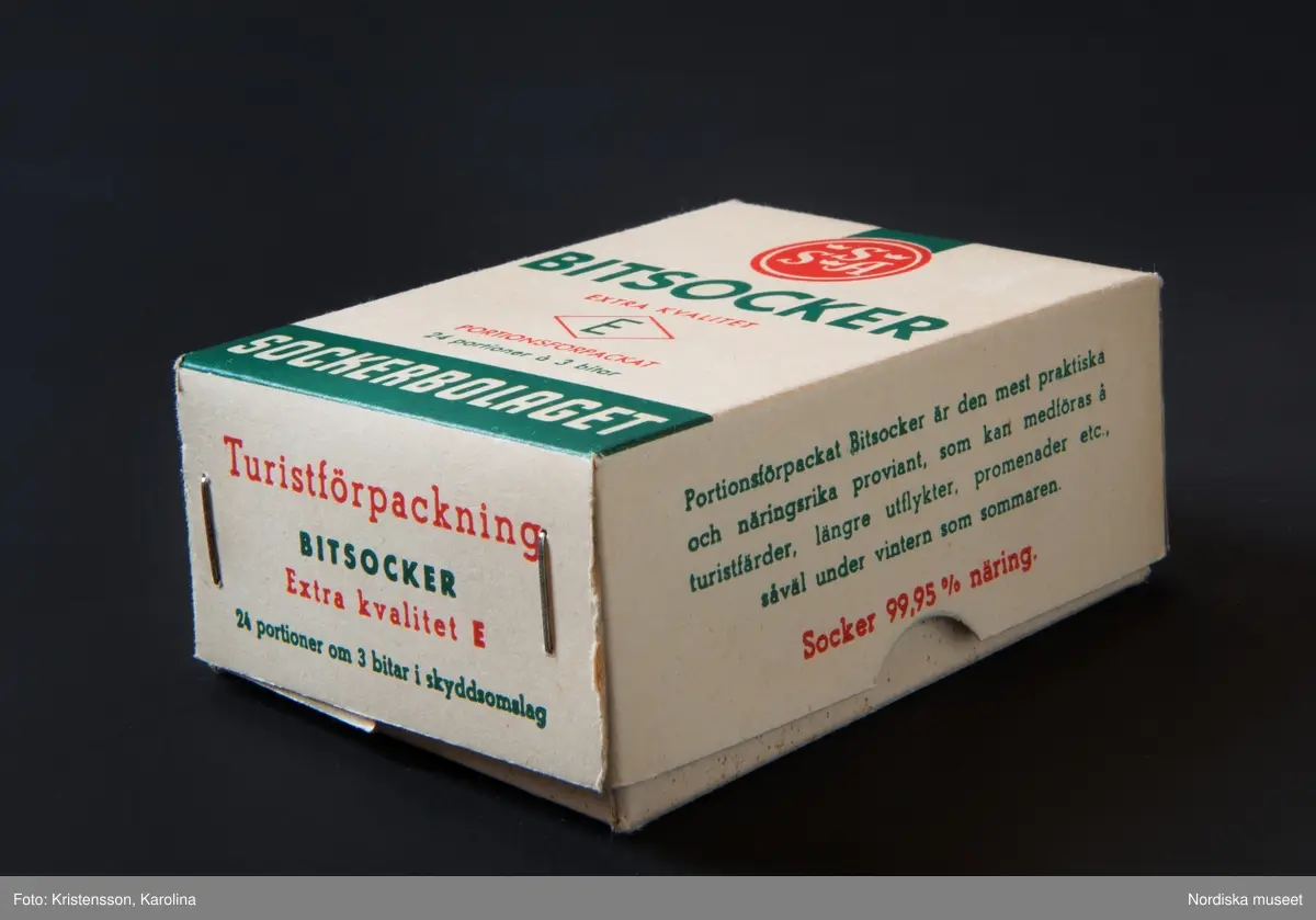 Huvudliggaren år 1960: 
”Ask, av kartong, överfalsat lock, alla hörn med häftade flikar; för ’Bitsocker extra kvalitet E portionsförpackat, 24 portioner á 3 bitar. Turistförpackning. Svenska Sockerfabriks AB.’ L 9,8 cm, Br 7,4 cm, Tj 3,8 cm. Gåva den 30/8 1960 av Fru Elsa Lindberg, Stockholm.”