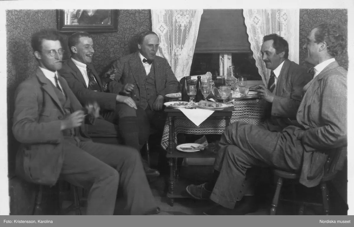 Fem män sitter runt ett bord på Älvdalens gästgivaregård och äter en måltid. från vänster fotograf Olle Ekberg, fil. dr. Bertel Hintze, intendent Sigurd Erixon (expeditionens ledare), antikvarien Ola Bannbers och arkitekt Mogens Mogensen. Bilden är tagen under Sigurd Erixons expedition i Ovansiljan 1926.