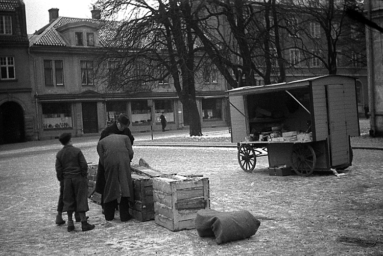 En man säljer potatis till några kunder. I bakgrunden ser man några av de dåv. husen längs Kungsgatan.