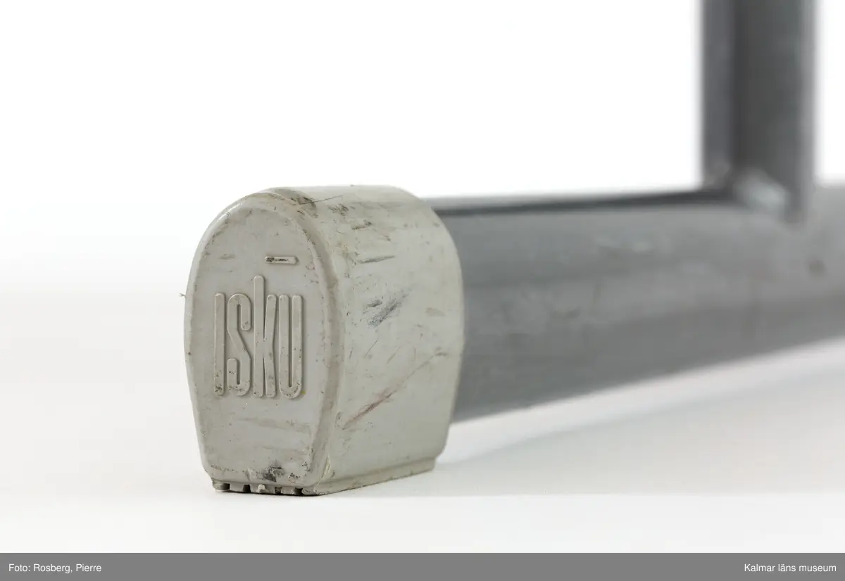 KLM 45904:1. Bänk, skolbänk. Av trä med metallunderrede. Uppfällbar ovansida med gulgrön färg. Skåra på ovansidan längst fram för pennor. Inuti och på sidorna rödmålad. På benen präglad text: ISKU. På framsidan skriver med blyerts: Jens Körge.