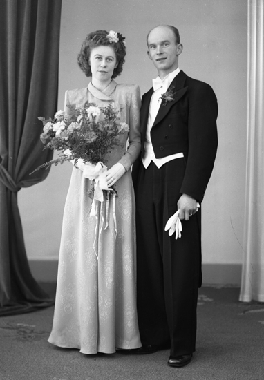 Foto av ett brudpar. Hon är klädd i färgad, mönstrad brudklänning utan slöja, men med blommor i håret.
Han bär frack.
Helfigur. Ateljéfoto.
Lars Gustaf Petersson (1917-     ), Alvesta. Gift 16 mars 1947 i Alvesta med Ingrid Margareta Kristina, f. Nilsson (1920-    ).
Källa: Vigselbok, Alvesta 1947.