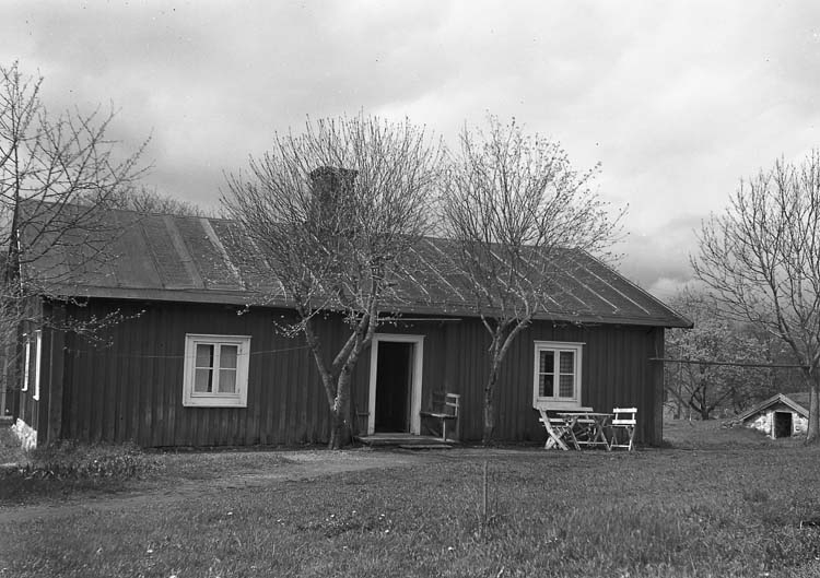 En stuga från Kosta.
Framför huset syns ett antal stolar och ett bord.